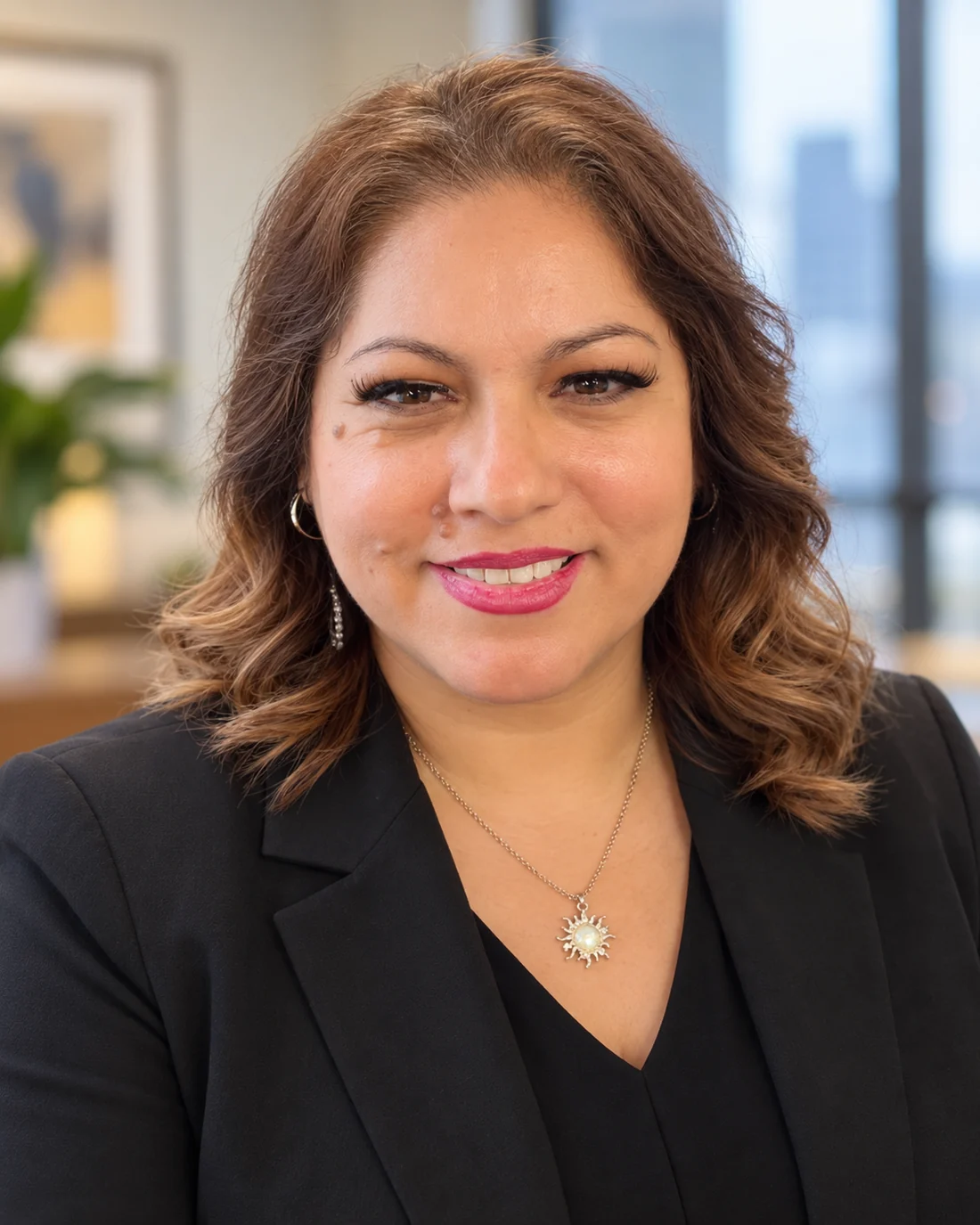 Karla Henry, smiling, in a black blazer with a gold sun pendant